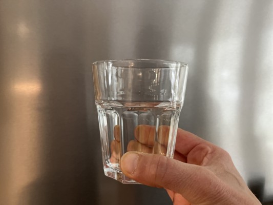 En hand håller i ett vattenglas.