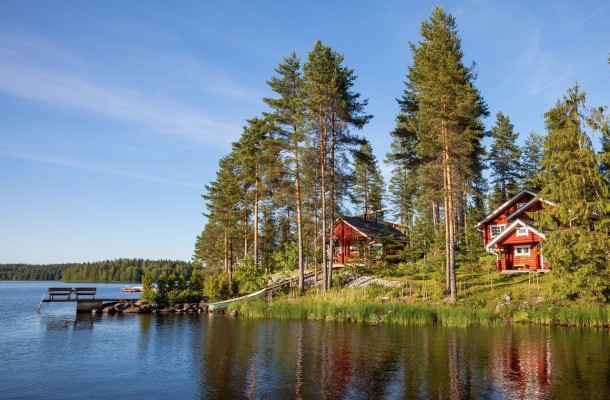 En röd sommarstuga med uthus på en udde vid en insjö.