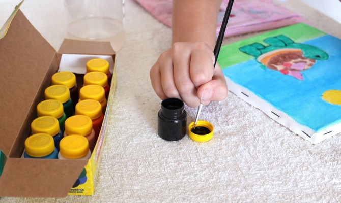 En barnhand håller i en pensel och doppar penseln i färgen.