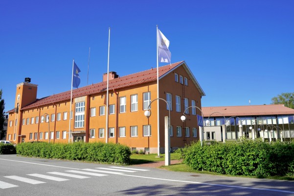 Kunnantalo Pännäisissä kuvattu aurinkoisena kesäpäivänä. Kunnan oma lippu heiluu tuulessa talon edessä.