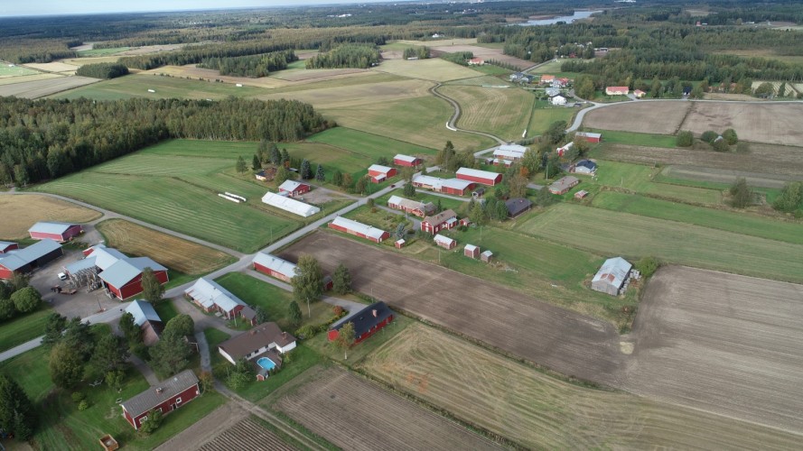 Flygbild över Östensö. Vägen genom byn och hus på sidan om vägen. Åkrar och lite skog.