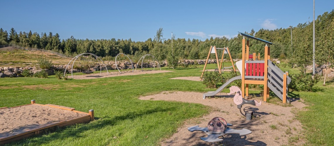 En lekpark med sandlåda, rutschkana, gungor och gungbräde.