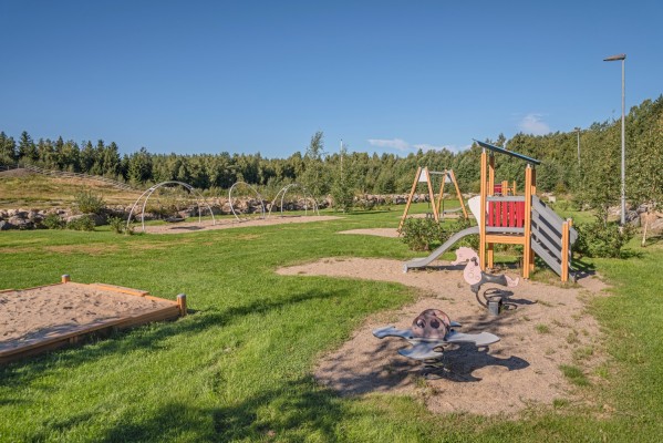 En lekpark med sandlåda, gungor och rutschkana.