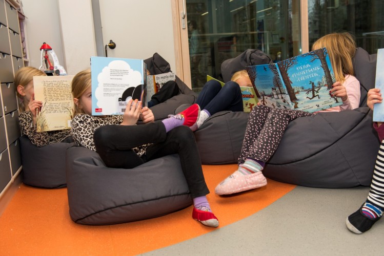 En grupp barn sitter och läser böcker i mysstolar.