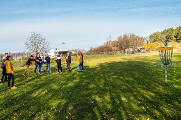 Koululaiset pelaavat frisbeegolfia nurmikentällä.