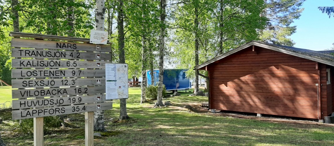 Saukonreitin opastetaulu Narsin uimarannan kohdalla. Taustalla pieni rakennus.