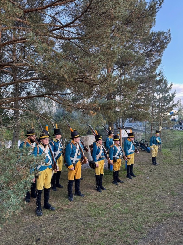 Ett fotografi av en trupp soldater med musköter på axeln från Oravais historiska förening som står framför minnesstenen. 
