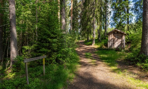 En bred stig i skogen och till höger ett utedass. På en skylt står: Skaldernas stig.