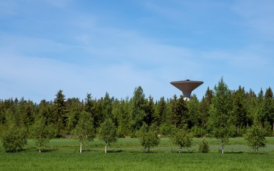 Vattentornet höjer sig över trädtopparna. I förgrunden ett gräsfält.