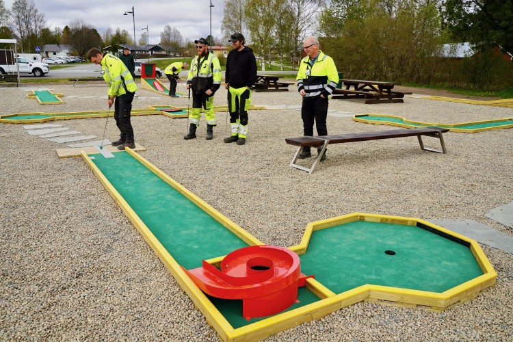 En man spelar minigolf på den nya planen i Bennäs. Fyra personer ser på.
