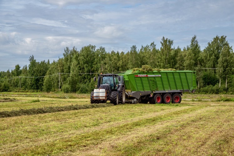 En traktor med ett gräslass på kärran kör på en åker.