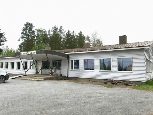 Ett lågt , avlångt hus med träpanel. Lite lösa brädor ligger på marken. Ovanför entrén finns en skylt med texten Purmogården.