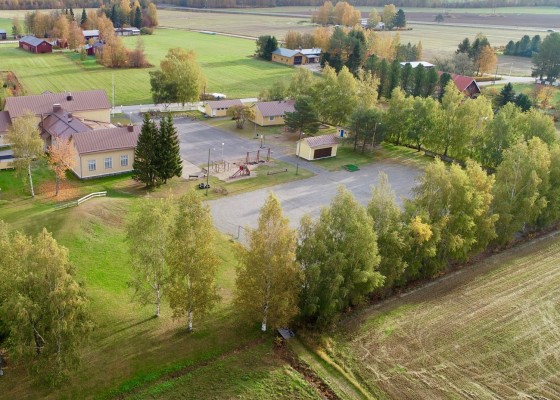 Östensö skolgård fotograferad med drönare. Skolfastigheten ligger till vänster, bredvid finns en stor grusplan. Också den lilla byggnaden som kallas Bryggan syns. Bredvid skoltomten går en väg.