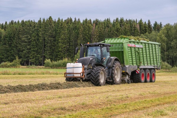 En traktor med släpkärra samlar in ensilage på en åker.