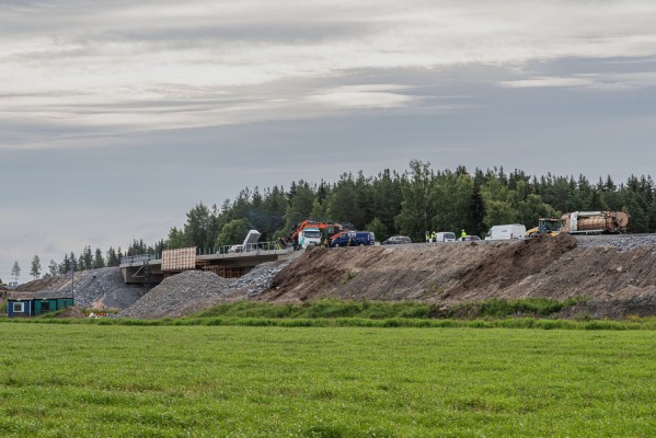 Uusi rautatien ylikulkusilta kuvattu pellolla. Sillalla rakennuskoneet ovat käynnissä.