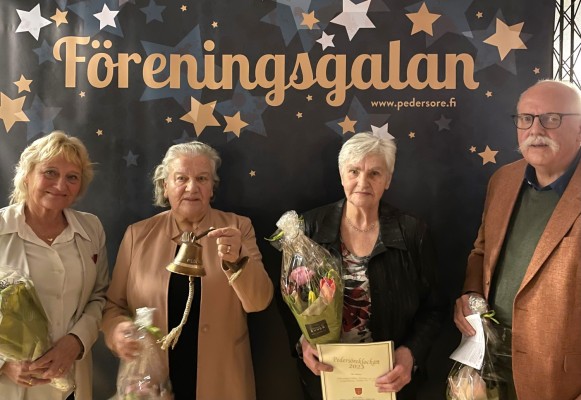 Fyra personer står mot en fondvägg med texten Föreningsgalan bakom sig. En kvinna håller en klocka i handen, alla har en blombukett i händerna.