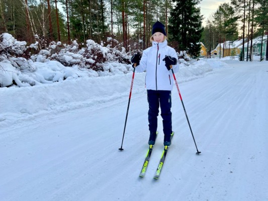 En flicka står på skidor med skidstavar i hand, på en snöklädd väg.