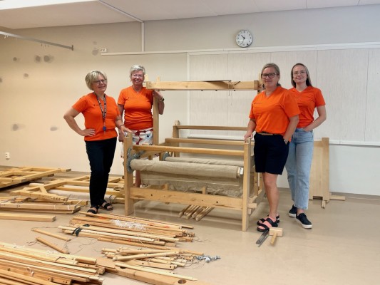 Pedersöre MI:s fyra anställda står runt en vävstol i den nya kurslokalen i Edsevö. På golvet ligger delar till flera vävstolar, ännu omonterade.
