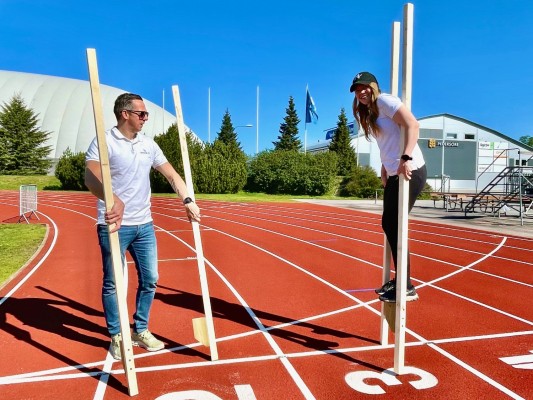 Idrottsekreteraren Pontus håller i ett par styltor och motionsrådgivaren Julia går på styltor. De är på friidrottsplanen i Bennäs.