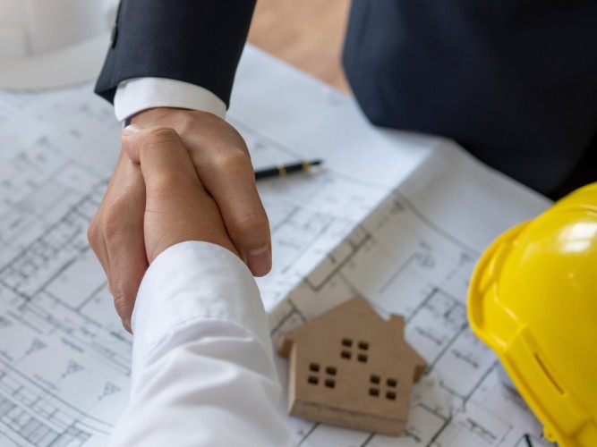 Två personer skakar hand. Det syns lite av en bygghjälm.