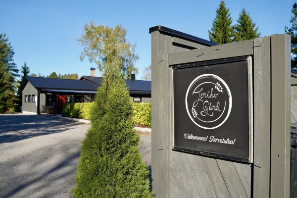 Ett staket med en skylt där det står Jeriko gård. I bakgrunden syns huset där bageriet finns.