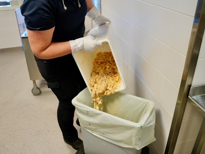 En person häller sopprester i ett avfallskärl med bioavfallspåse.