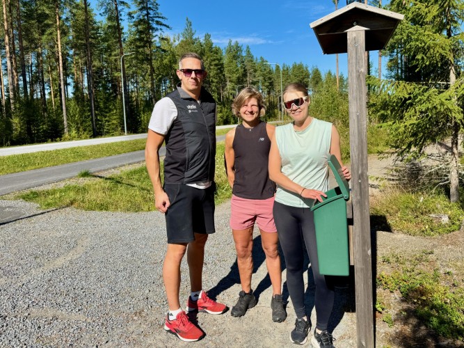 En man och två kvinnor står vid en motionslåda, som ligger intill en väg.