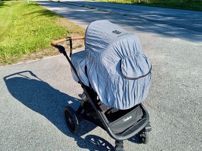 En barnvagn iklädd en reflexhuva, som täcker hela vagnen. Vagnen står utomhus på en väg.