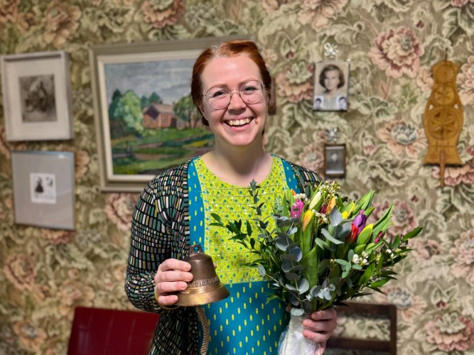 Charlotta Kerbs håller i blombukett och kulturpriset, en vällingklocka, och ler stort mot kameran.