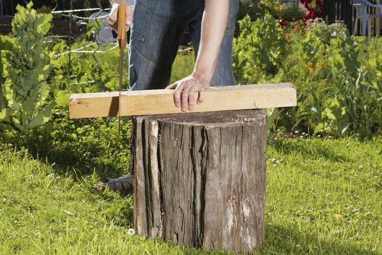 En person sågar en tjock bräda i en trädgård.