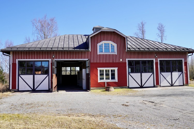 Den aktuella verkstadsbyggnaden. Fyra dubbla dörrar, varav en är öppen. Två fönster ovanpå varandra. Byggnaden har två våningar i mitten. 