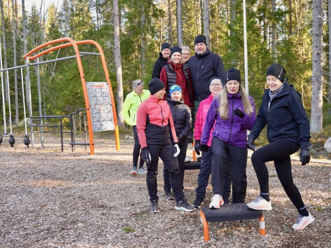 Hela ledningsgruppen plus kommunens två rörelsecoacher står fritidsklädda i utegymmet i Sandsund. De två personerna längst fram kliver upp på en "pall". Alla är glada.