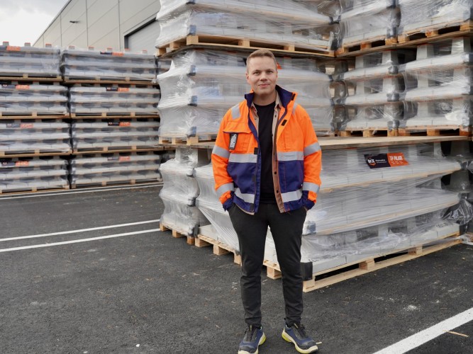 VD:n Tobias Hjulfors står utomhus framför lastpallar fyllda med betongplintar.