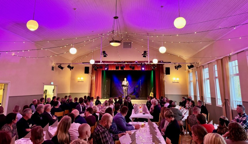 En festlokal med dämpad belysning. Folk sitter kring långbord.