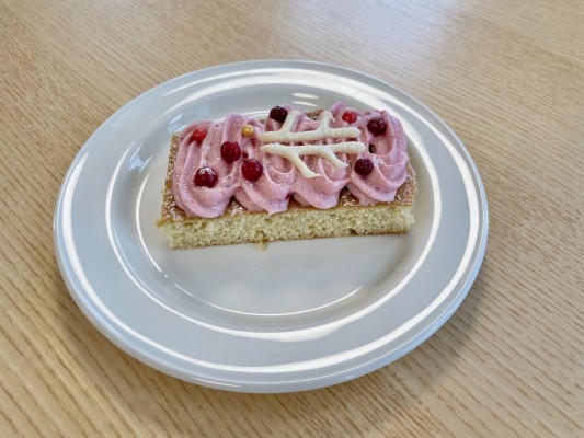 Ulla-Hjärdis kako, har en ljus botten och rosa glasyr, samt lingon och en spritsad Pedersörelogo överst.