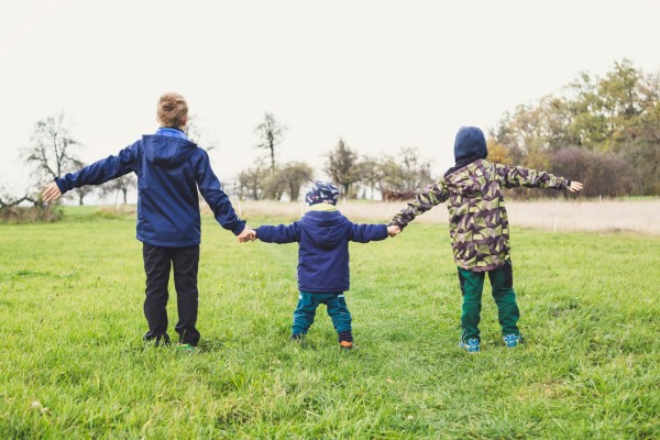 Tre barn håller varandra i händerna när de står på en stor gräsmatta.