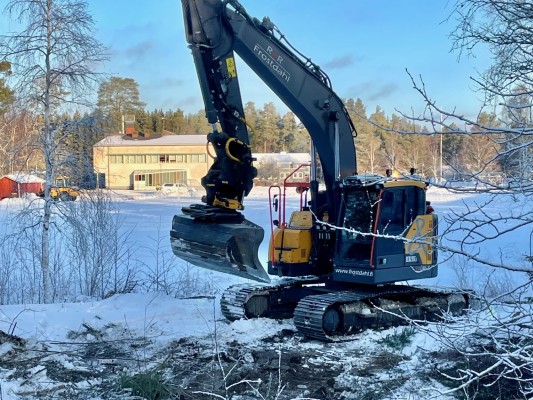 En grävmaskin gräver, i bakgrunden syns Sandsund skola.