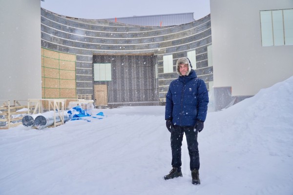 Taiteilija Jon Gredmark seisoo uuden Axåkers skolan rakennustyömaalla. Taustalla on tuleva koulurakennus. Maa on lumessa, ja lisää tulee taivaasta.