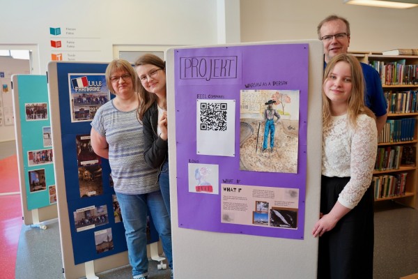 Bild från utställningen i huvudbiblioteket. Flickorna Emma och Agnes står på varsin sida av en informationsplansch, och bredvid dem står lärarna Camilla och Peter.