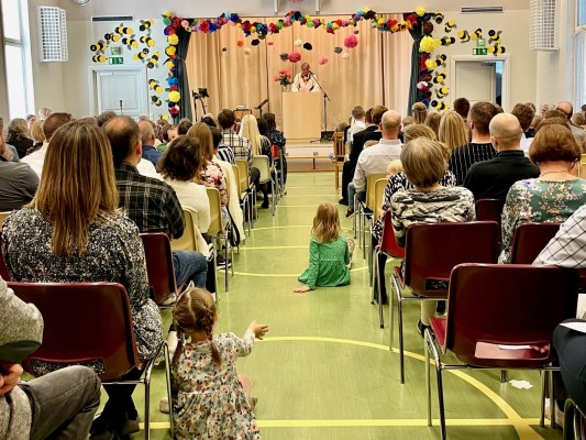 Festsalen i Östensö skola är fylld med folk. Salen är pyntad med pappersblommor i starka färger. Längst fram står tidigare rektorn Ritva och håller tal.