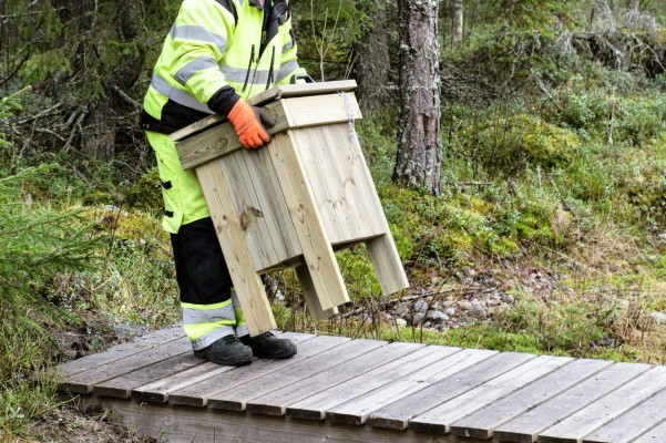 En person bär bort en hundbajslåda på en bro som går över ett dike.