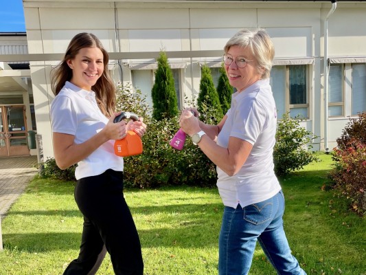 Kaksi iloista naista seisoo kettlebellit käsissään ulkona.