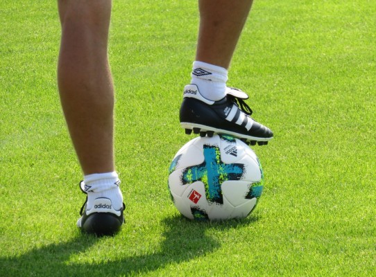 Lähikuvassa jalkapalloilija, jolla on yksi jalka pallon päällä.
