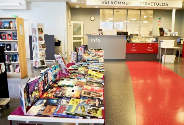 Bord fyllt med biblioteksböcker, lånedisk i bakgrunden.