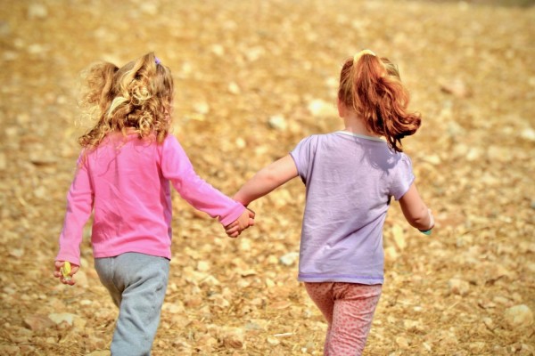 Två flickor springer utomhus och håller varandra i hand.