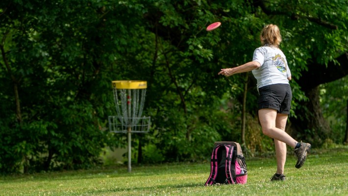 Person kastar frisbee mot en korg.