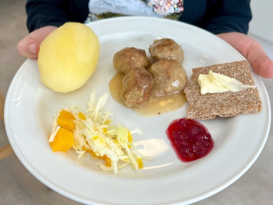 En tallrik med en stor potatis, fyra köttbullar, lite sallad, en klick lingonsylt och ett knäckebröd med smör.