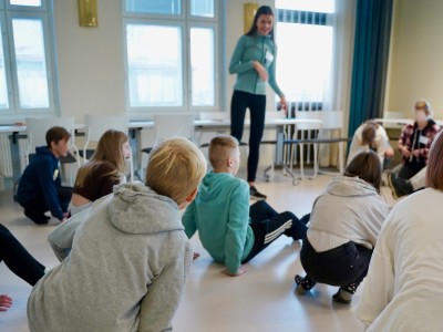 En vuxen står på golvet omgiven av barn som gympar.