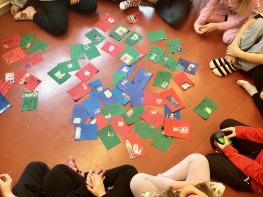 En massa kort i kartong är utspridda på golvet. Det syns knän av barn som sitter runt korten.