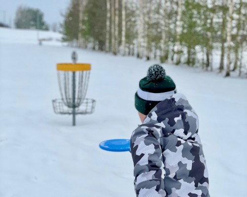 Ett barn kastar frisbee i en korg. Det är vinter.